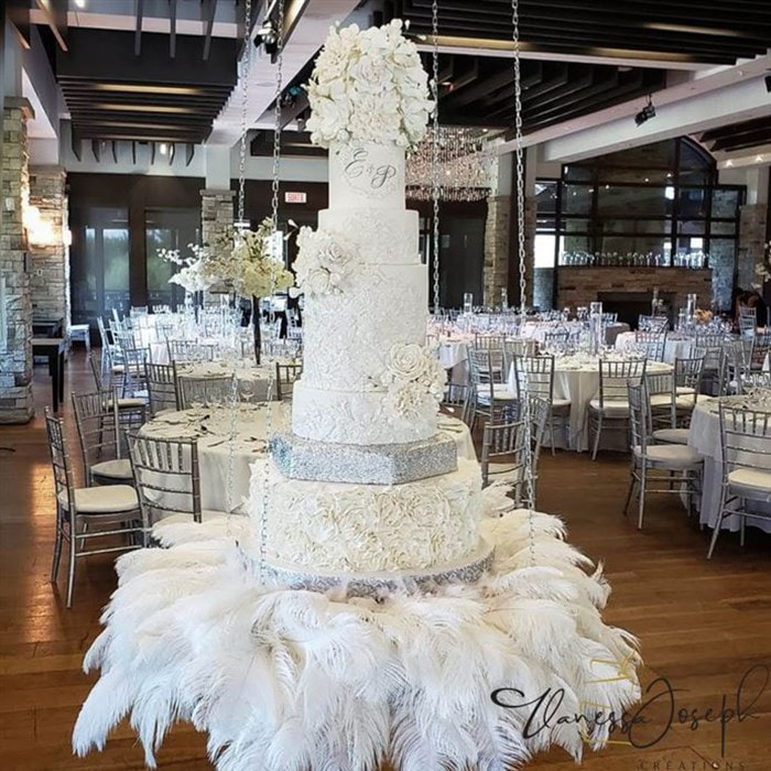 white and silver wedding cake on a hanging table with white feathers