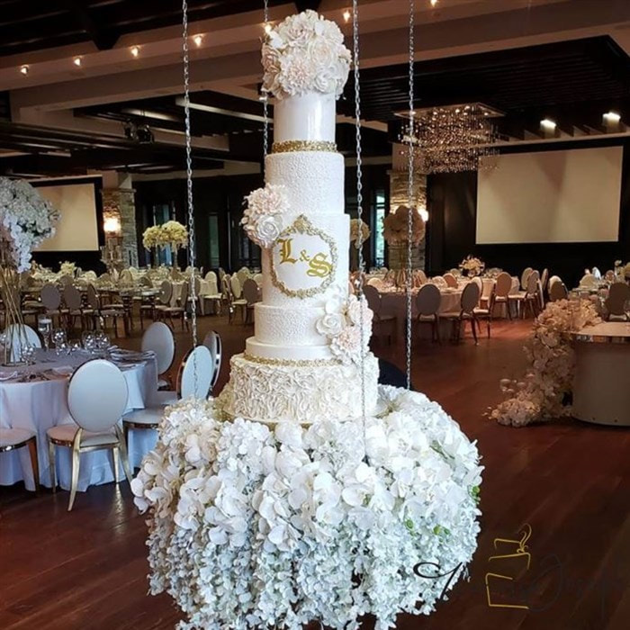 white and gold royal theme wedding cake on a hanging table with flowers 