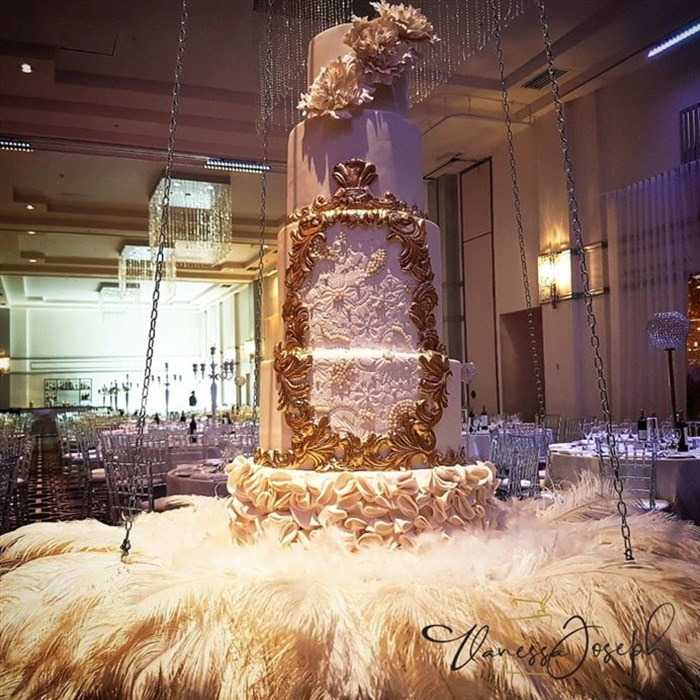 royal white and gold wedding cake on hanging table with white feathers