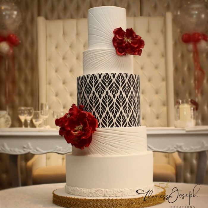 white wedding cake with black and white pattern and bright red flowers