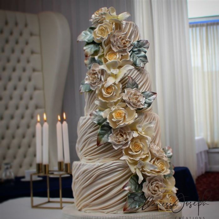 Draped white wedding cake with white and yellow cascaded flowers 