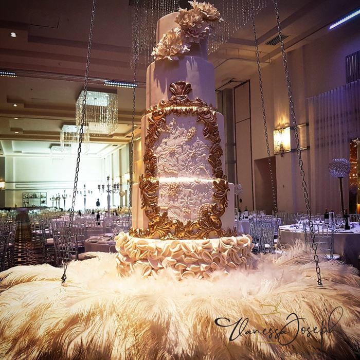 gâteau de mariage royal blanc et or suspendu sur des plumes blanches